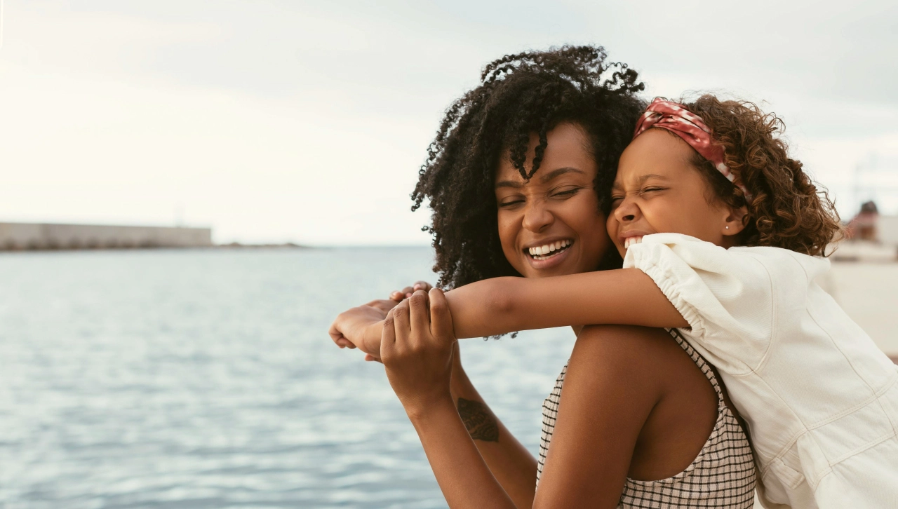 Smiling mother holding small child on her back with view of water in the background